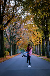 Full length of couple embracing while standing amidst trees on road