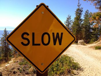 Close-up of slow sign by dirt road against blue sky