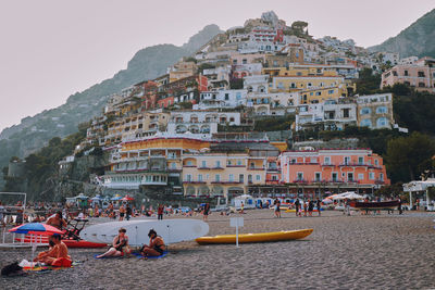 People on beach by buildings in city against sky