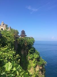 Uluwatu temple on mountain by sea against blue sky