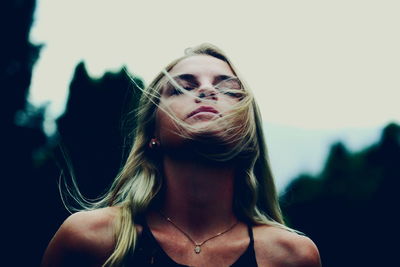 Woman with closed eyes and tousled hair against sky