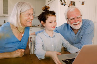 Girl showing laptop to smiling grandparents at home