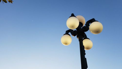 Low angle view of illuminated lighting equipment against clear blue sky