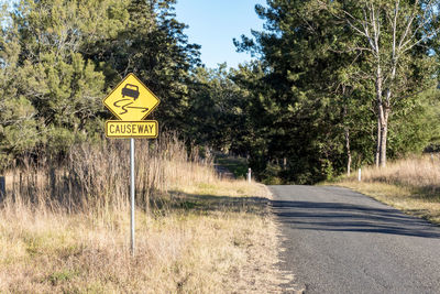 Road sign by trees against sky