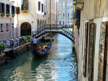 People in boat by bridge over canal against buildings