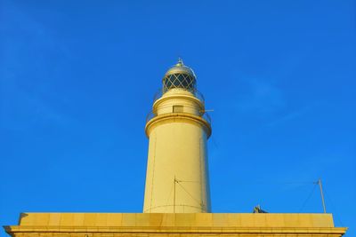 Low angle view of lighthouse against building against clear blue sky