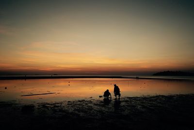 Silhouette people at beach against sky during sunset