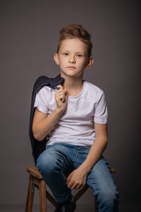 Boy sitting on stool against black background
