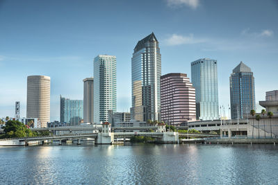 Modern buildings by river against sky in city