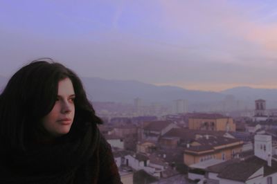 Thoughtful woman against townscape during sunset