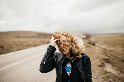 Portrait of young woman with umbrella standing on road against sky