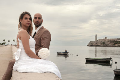 Young couple sitting on shore against sky