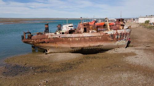 Abandoned boat moored on beach against sky