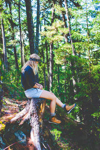 Side view of woman sitting on tree stump in forest