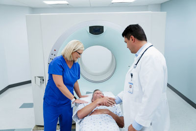 Doctor shaking hands with patient lying by nurse for mri scan in examination room