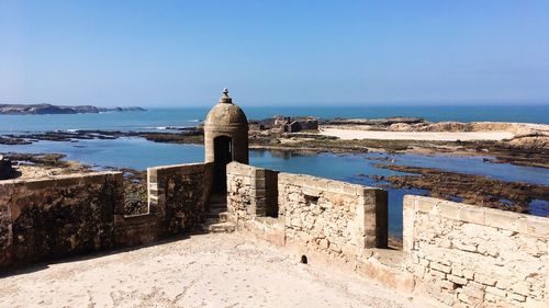 Built structure by sea against clear blue sky