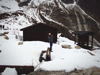 Full length of woman standing by hut on snowcapped mountain