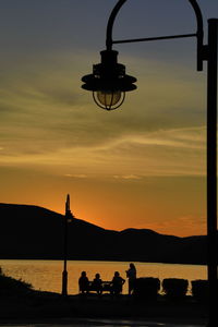 Silhouette people on street against orange sky