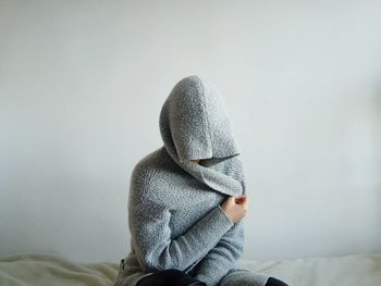 Person wearing warm clothing sitting on bed against wall