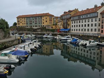 Sailboats moored on canal amidst buildings in city against sky