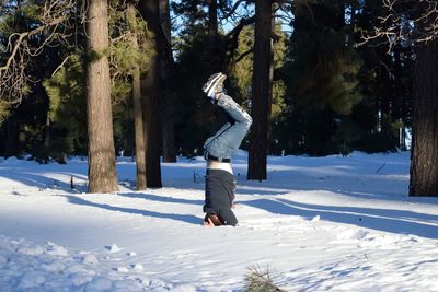 Man doing handstand on snow against trees