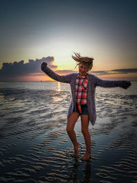 Woman standing at beach against sky during sunset