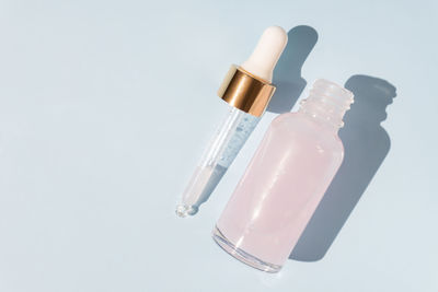 Top view of transparent dropper bottle with pink beauty face oil on blue background. anti aging