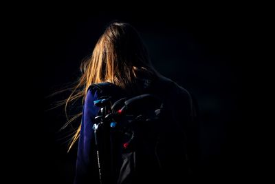 Rear view of backpack woman standing against black background