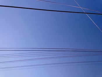 Low angle view of electricity pylon against clear blue sky