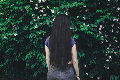 Rear view of woman standing by trees on field