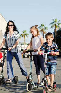 Happy family lifestyle. mother, boy, girl in city. ride scooters. laughing on a summer. fun