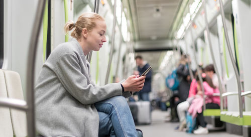 Side view of woman using smart phone sitting in subway train