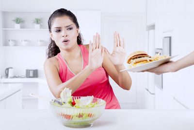 Woman with salad bowl denying burger at home