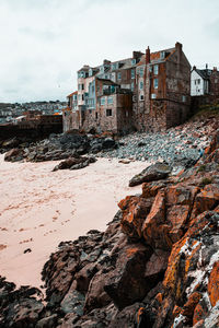 Rocks on beach by buildings against sky