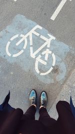 Low section of person standing by bicycle sign on road