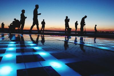 Silhouette people by swimming pool against sky during sunset