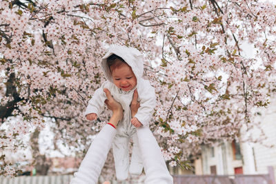Happy cute girl held by cropped mother against cherry blossoms