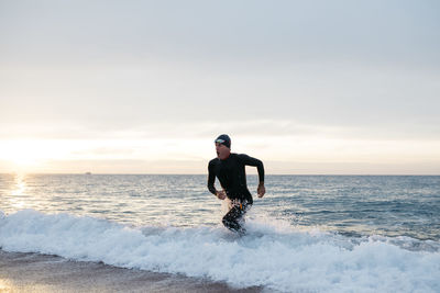 Rear view of man standing at beach against sky during sunset