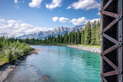 Scenic view of turquoise river in forest against mountains and blue sky