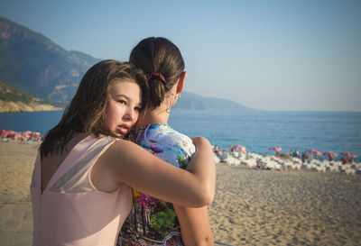 Girl embracing mother while standing on sand at beach