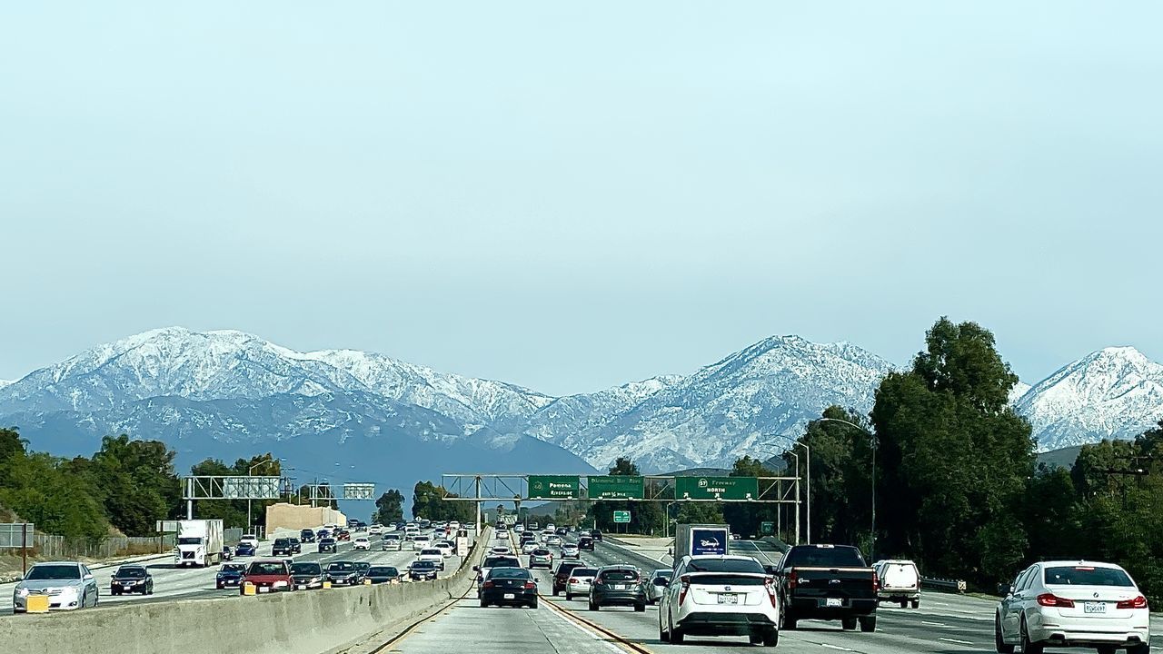 CARS ON ROAD AGAINST SNOWCAPPED MOUNTAINS