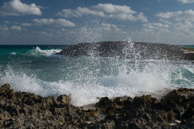 Waves splashing on rocks at shore against sky