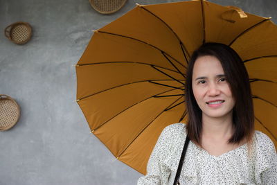 Portrait of smiling woman holding umbrella against wall