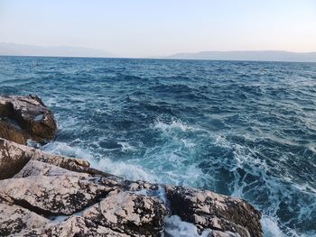 Waves splashing on rocks against clear blue sky