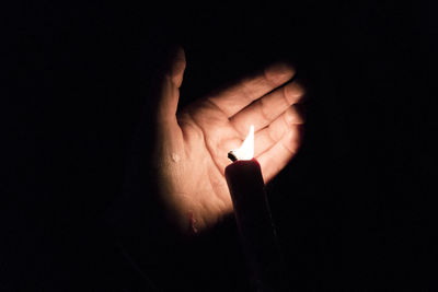 Cropped hand with lit candle in darkroom