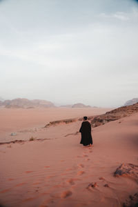 Rear view of man walking at desert against sky during sunset