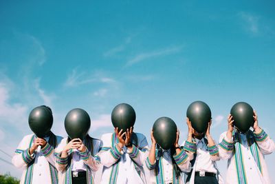 People holding balloons by face against blue sky