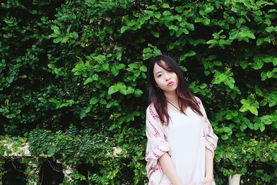 Beautiful young woman standing by ivy on tree