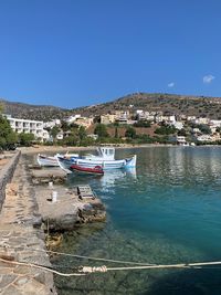 Boats moored at harbor against clear blue sky