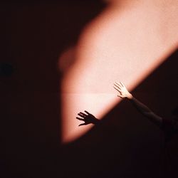 Cropped hand of person reaching for sunlight in darkroom